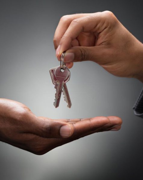 Close-up Of Hands Giving Keys Of An Apartment Against Gray Background